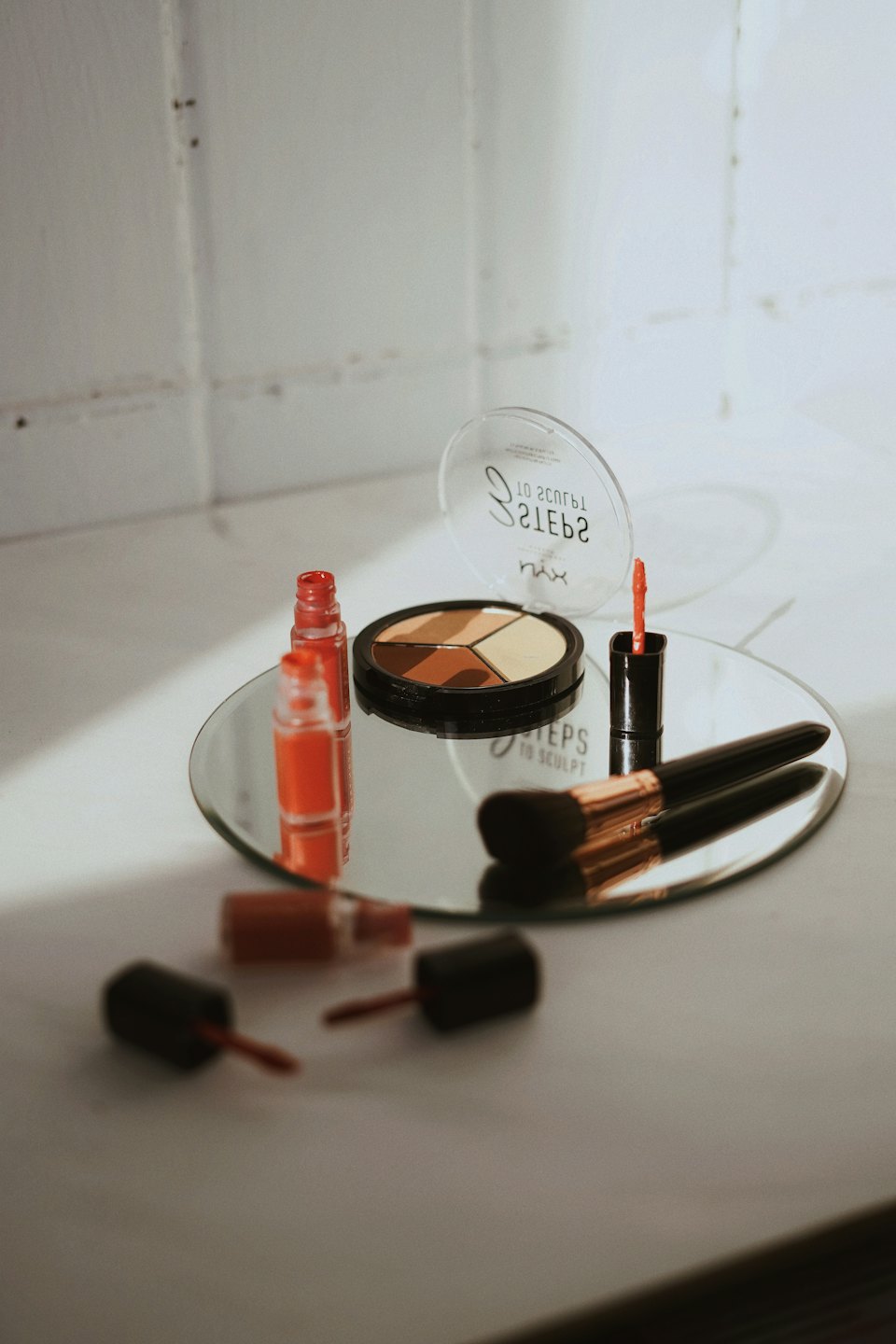 Makeup products and brush on a mirrored tray.