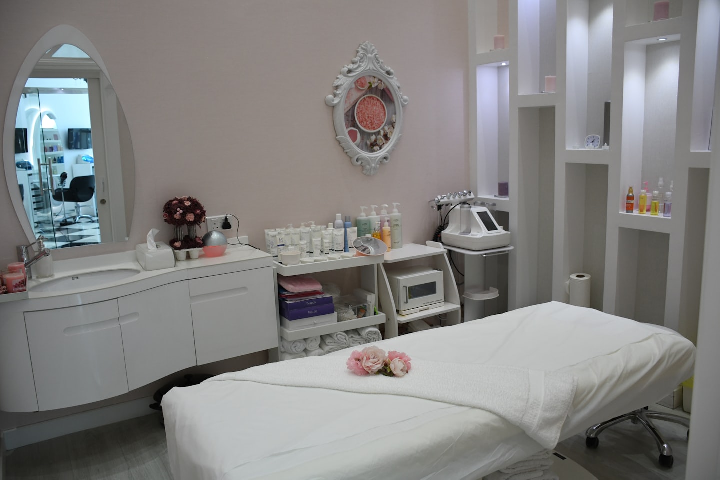 Clean beauty salon treatment room with white bed and pink flowers.