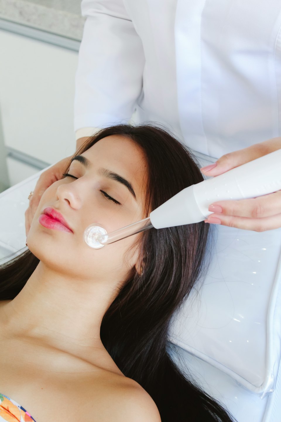Hands perform a high-frequency facial treatment with a glowing electrode.